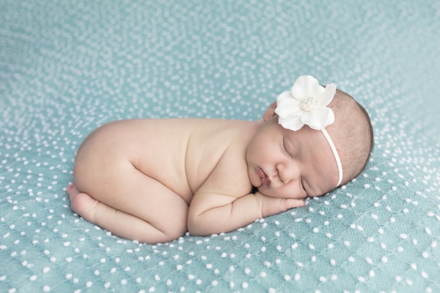 Baby girl posed bottom-up on teal blanket with white polka dots with white flower headband for newborn portrait session