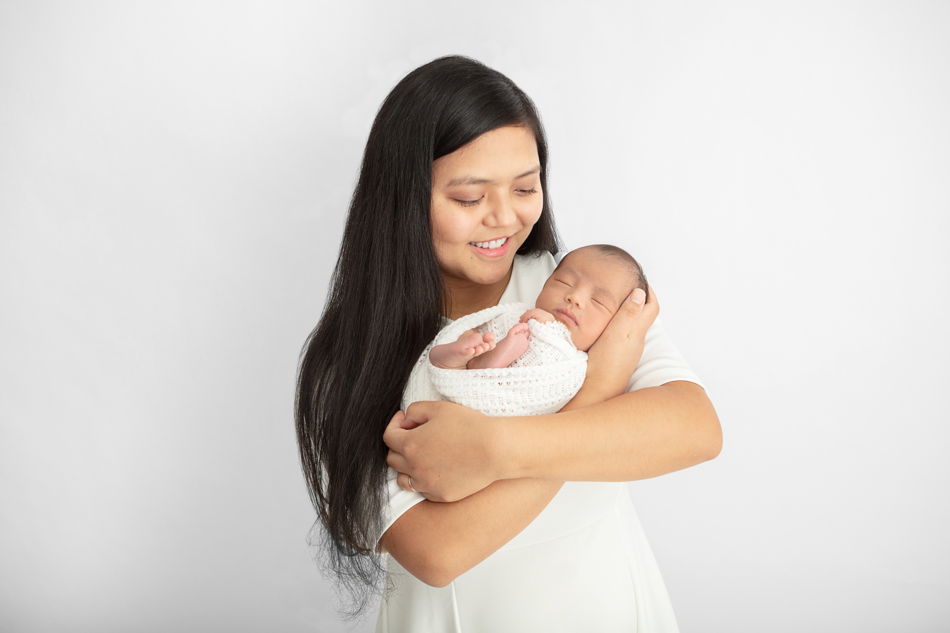 mother with long black hair smiling down at her newborn baby girl who is being cradled in her arms