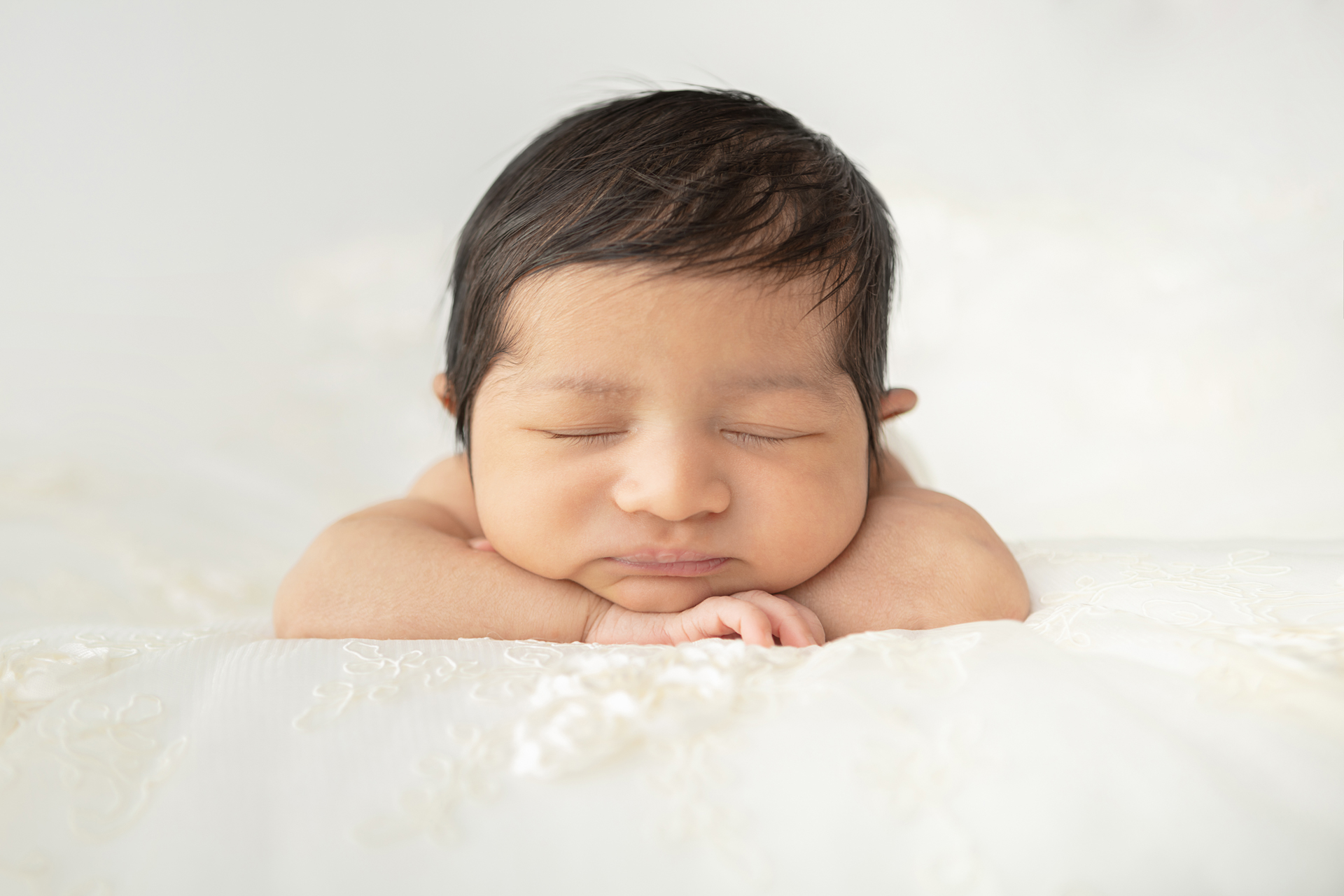 newborn baby girl with a head full of dark hair asleep with her head resting on her folded arms
