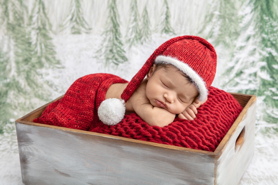 newborn baby wearing a Santa stocking cap and wrapped in a red chenille blanket