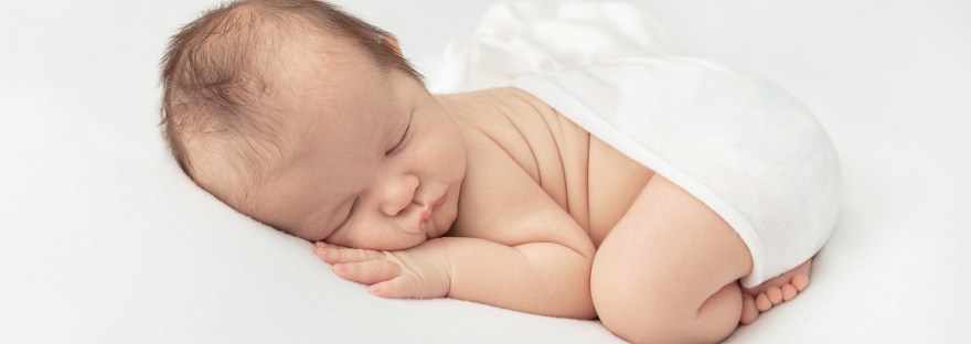 newborn baby boy asleep on a bed of white, swaddled in white