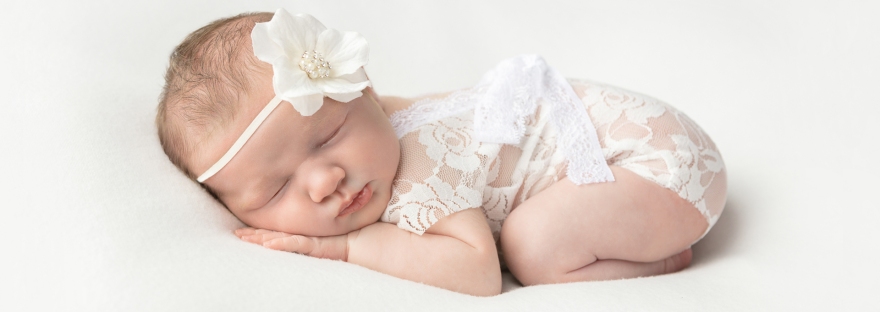 newborn baby girl in lace onesie and wearing a large white flower headband