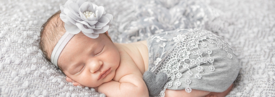 newborn baby girl swaddled in gray wearing a gray floral headband