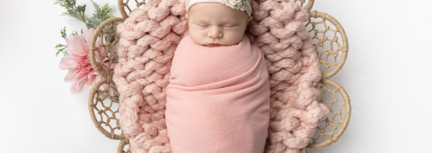 newborn girl wrapped in a dusty pink swaddle asleep on a chunky knit blanket