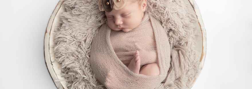 newborn baby girl loosely swaddled in neutral knit blanket